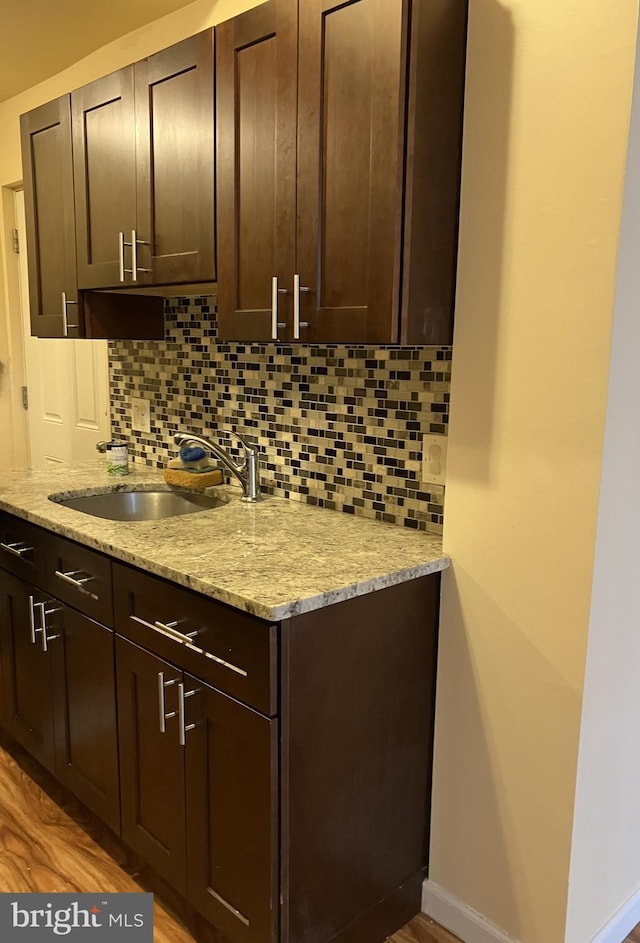 kitchen with decorative backsplash, sink, dark brown cabinetry, and light stone counters