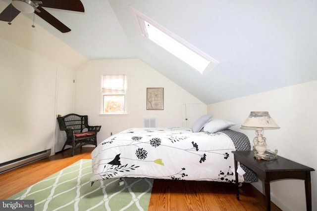 bedroom featuring hardwood / wood-style flooring, lofted ceiling with skylight, ceiling fan, and baseboard heating