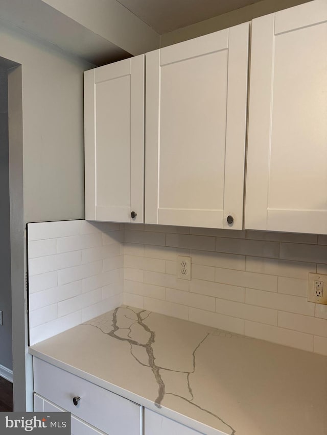 interior space with white cabinetry, backsplash, and light stone counters