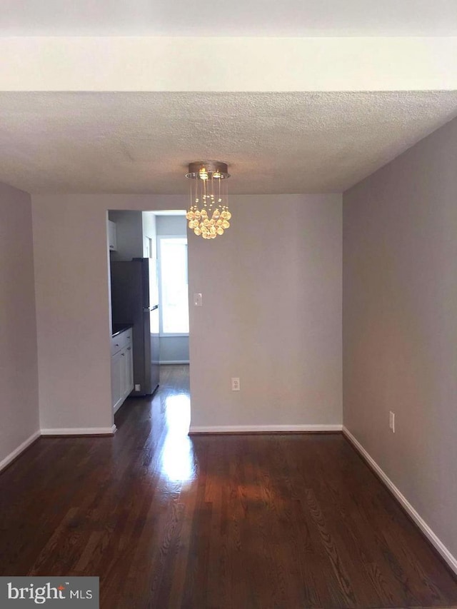 spare room with a chandelier, a textured ceiling, and dark hardwood / wood-style flooring