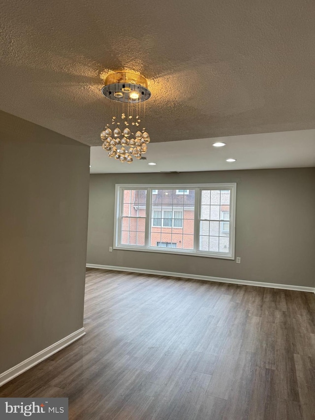 empty room with dark hardwood / wood-style flooring, a textured ceiling, and a notable chandelier