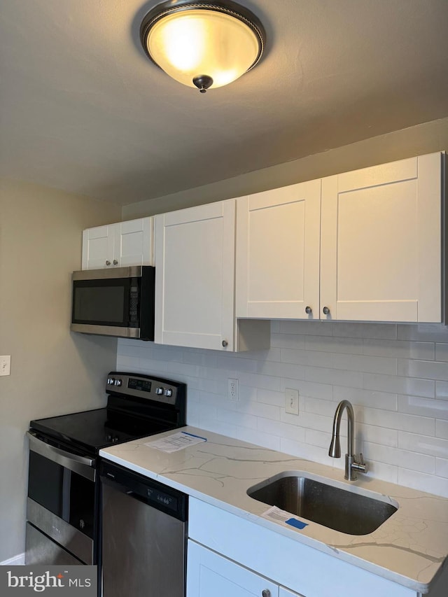 kitchen featuring sink, tasteful backsplash, stainless steel appliances, light stone countertops, and white cabinets