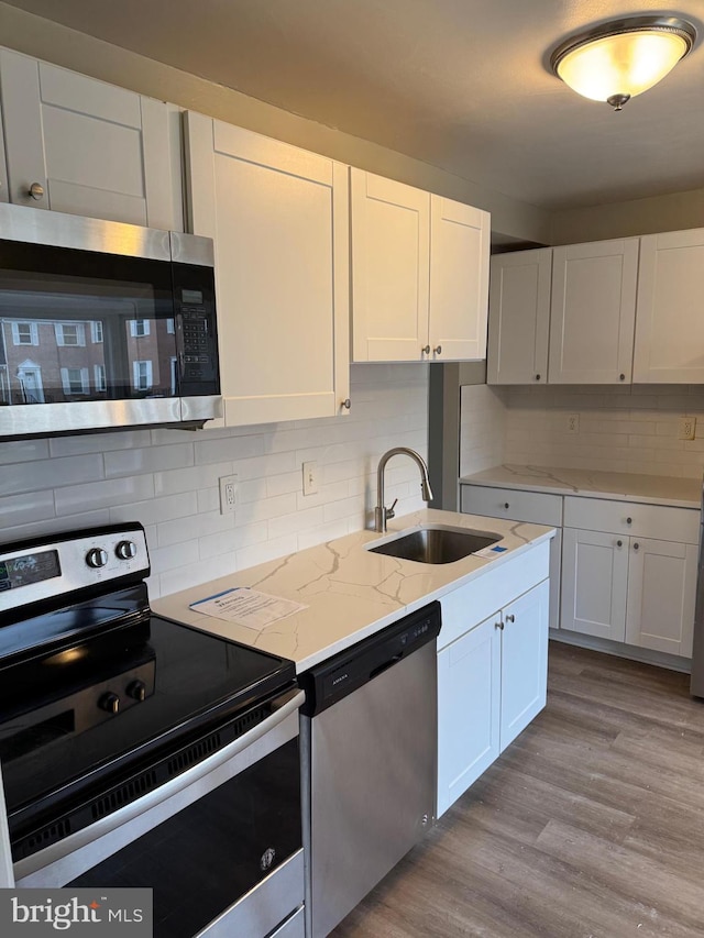 kitchen featuring sink, white cabinetry, stainless steel appliances, light stone countertops, and light wood-type flooring