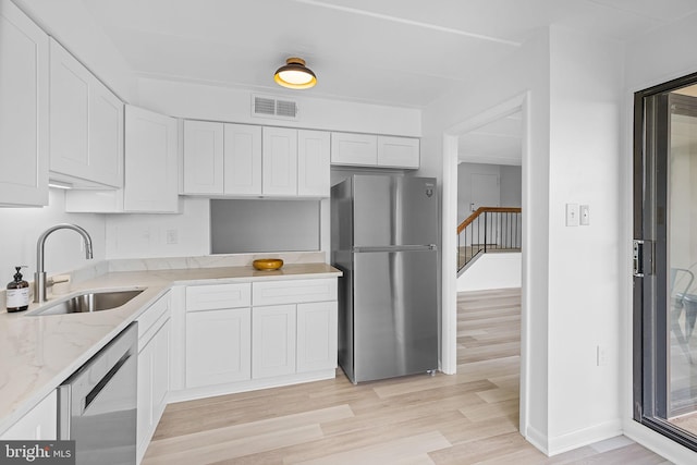 128 Roberts Ln Unit 301, Alexandria, VA 22314 - kitchen with stainless steel appliances, a sink, light stone counters, white cabinets, and light wood-type flooring