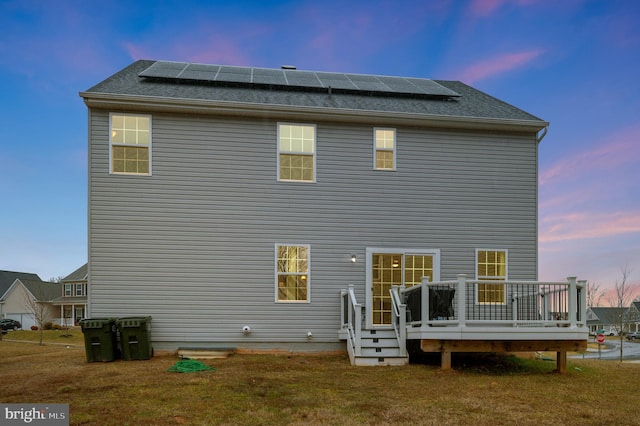 back house at dusk featuring a yard, a deck, and solar panels