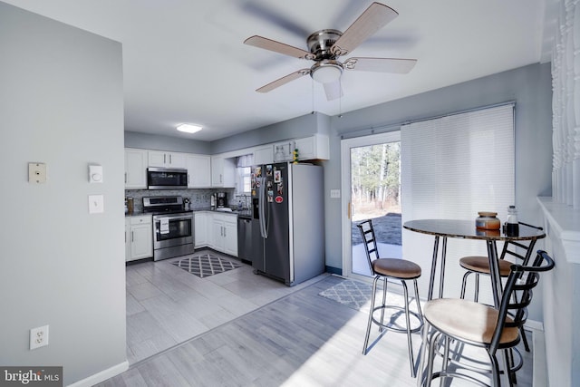 kitchen with sink, light wood-type flooring, appliances with stainless steel finishes, white cabinets, and backsplash