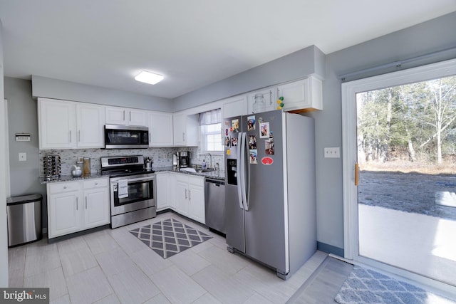 kitchen featuring sink, appliances with stainless steel finishes, white cabinets, dark stone counters, and backsplash