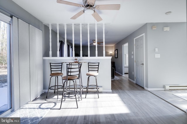 kitchen with baseboard heating, ceiling fan, a kitchen bar, and hardwood / wood-style flooring