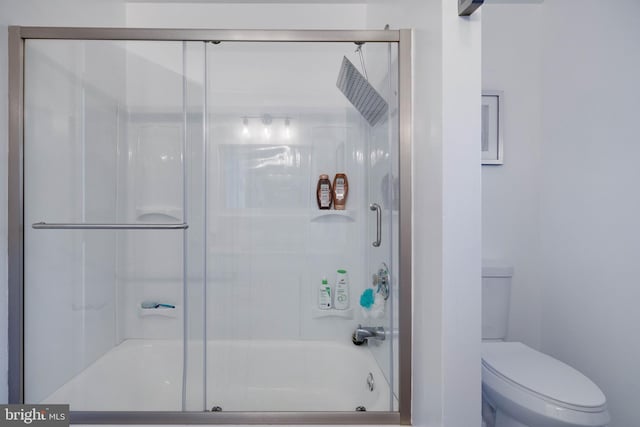 bathroom featuring toilet and bath / shower combo with glass door