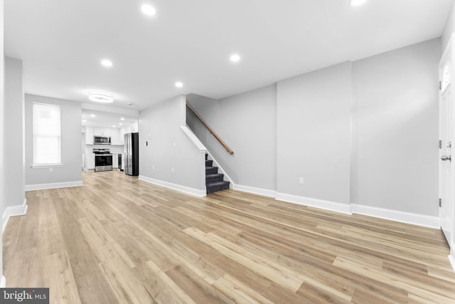 unfurnished living room featuring baseboards, stairway, light wood-style flooring, and recessed lighting