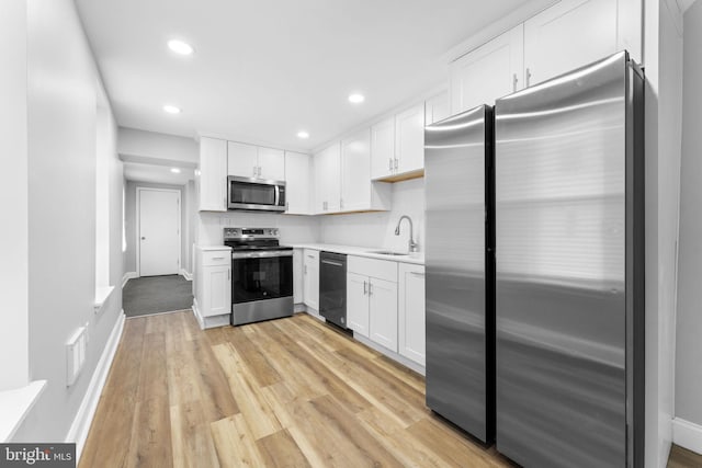 kitchen with light countertops, appliances with stainless steel finishes, white cabinets, a sink, and light wood-type flooring