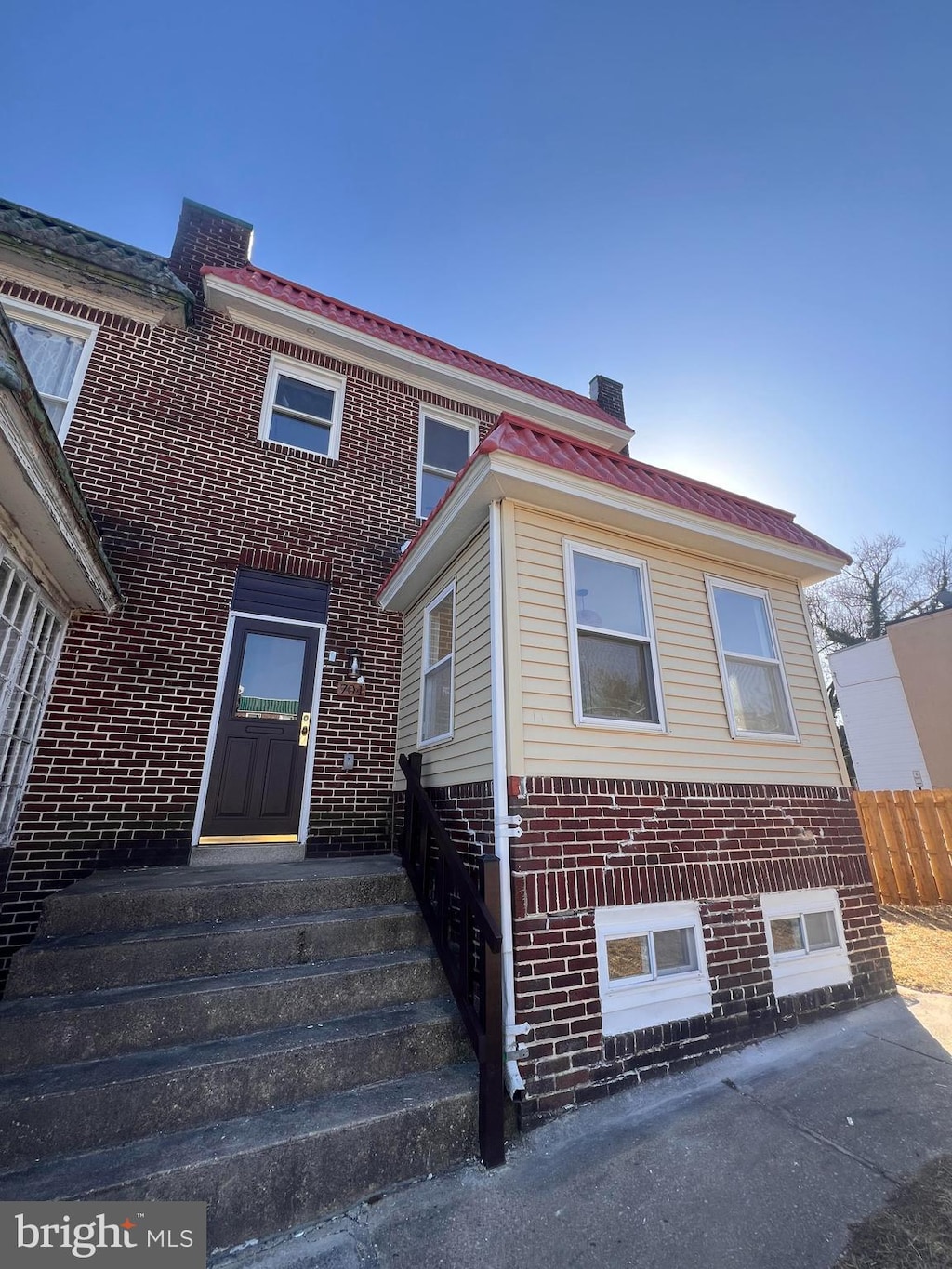 view of front facade featuring brick siding, a chimney, metal roof, and fence