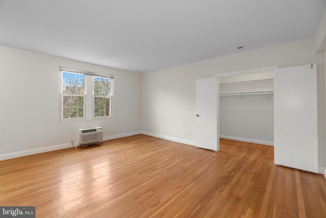 unfurnished bedroom with a closet, a spacious closet, wood-type flooring, and an AC wall unit