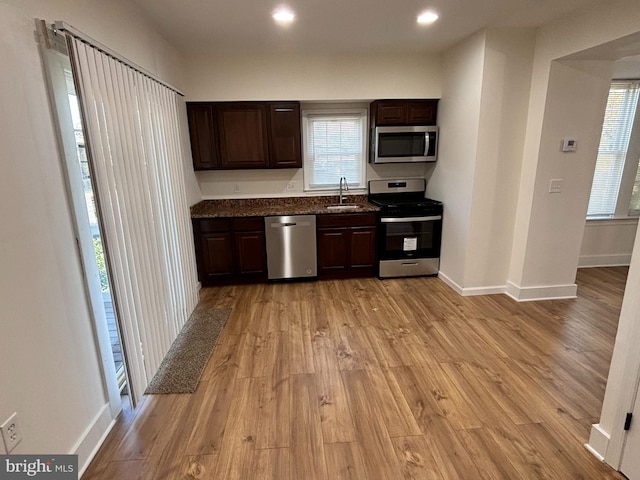 kitchen with sink, dark stone countertops, stainless steel appliances, dark brown cabinets, and light wood-type flooring