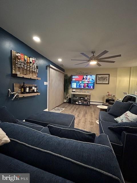 living room featuring wood-type flooring, a baseboard heating unit, and ceiling fan