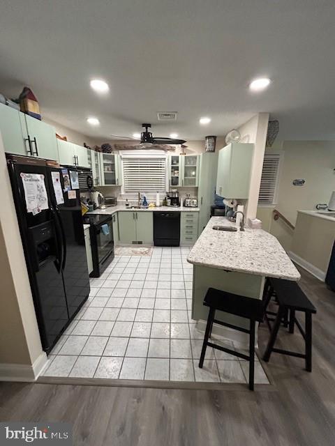 kitchen featuring sink, light hardwood / wood-style flooring, green cabinets, and black appliances