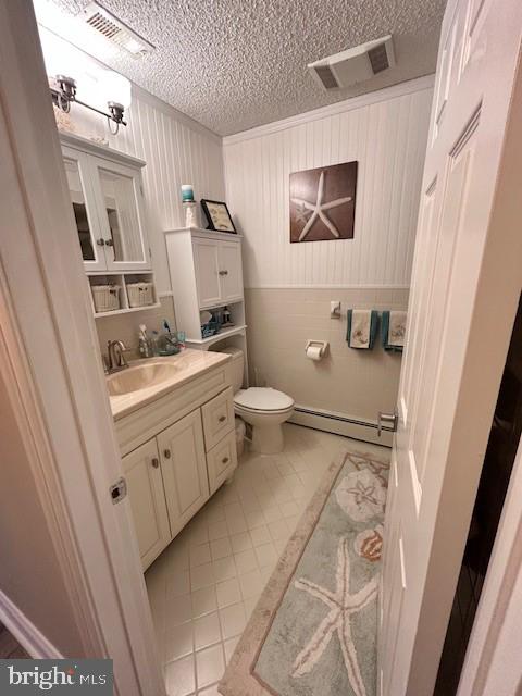 bathroom featuring vanity, ornamental molding, a baseboard heating unit, toilet, and a textured ceiling