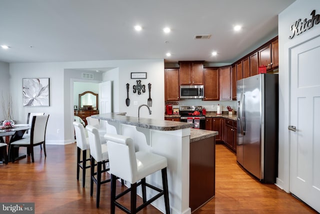 kitchen with light wood-type flooring, stainless steel appliances, a breakfast bar, and a center island with sink