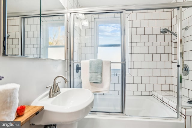 full bath with a wealth of natural light, shower / bath combination with glass door, and a sink