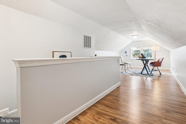 hall with lofted ceiling, wood finished floors, visible vents, and baseboards