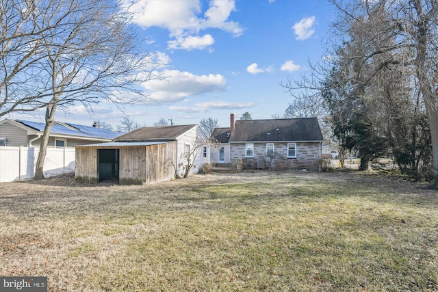 back of property featuring an outdoor structure, fence, a yard, stone siding, and a shed