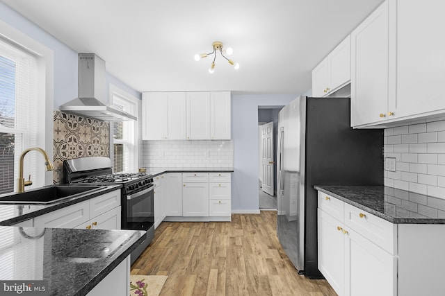 kitchen featuring wall chimney exhaust hood, sink, dark stone countertops, appliances with stainless steel finishes, and white cabinets