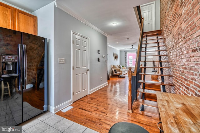 hall with crown molding, brick wall, and light hardwood / wood-style flooring