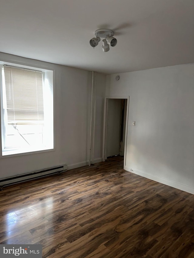 empty room featuring a baseboard heating unit and dark wood-type flooring