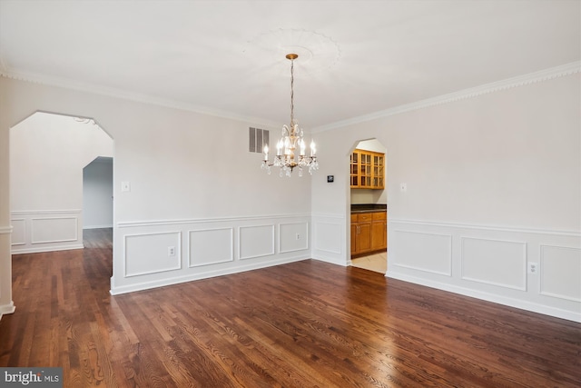 spare room featuring dark wood-type flooring, crown molding, and an inviting chandelier