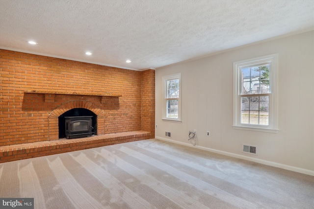 unfurnished living room with brick wall, carpet flooring, a textured ceiling, and a wood stove