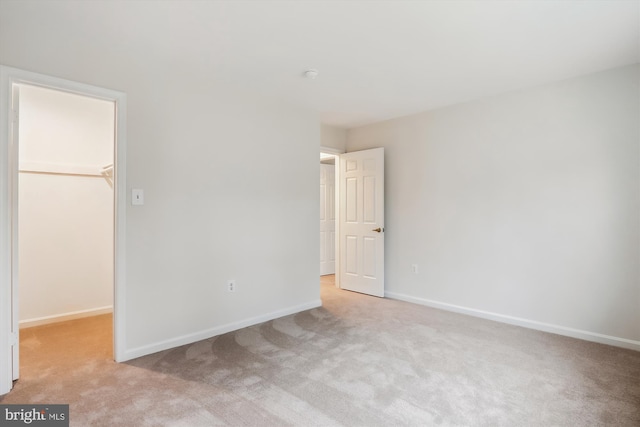 unfurnished bedroom featuring a closet, a spacious closet, and light carpet