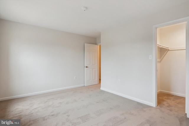 unfurnished bedroom with a walk in closet, light colored carpet, and a closet