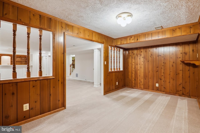 carpeted spare room featuring crown molding, a textured ceiling, and wood walls