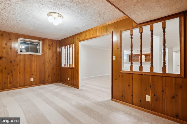 unfurnished room with light colored carpet, a textured ceiling, and wood walls