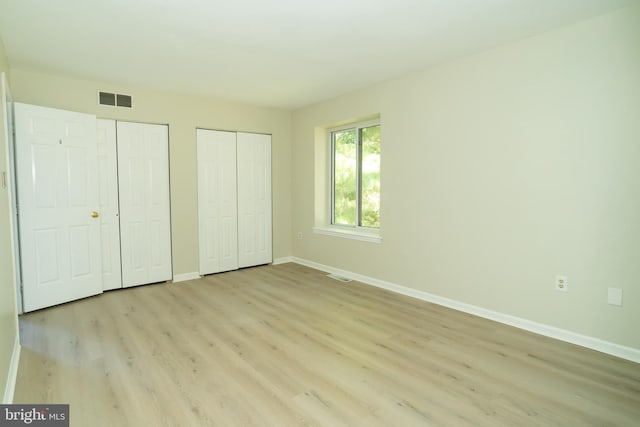 unfurnished bedroom featuring two closets and light wood-type flooring