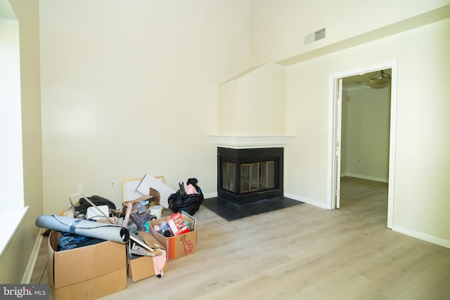 living room with light wood-type flooring, a high ceiling, and a multi sided fireplace