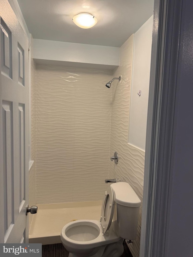 bathroom with tiled shower, tile walls, and toilet