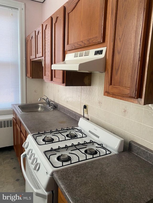 kitchen featuring white gas range, backsplash, radiator heating unit, and sink