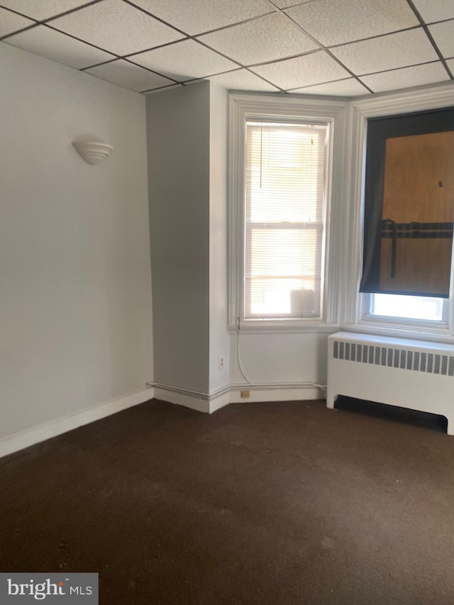 empty room with radiator heating unit, a drop ceiling, and dark colored carpet