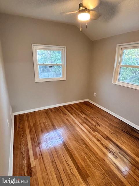 empty room featuring ceiling fan, hardwood / wood-style flooring, vaulted ceiling, and a textured ceiling