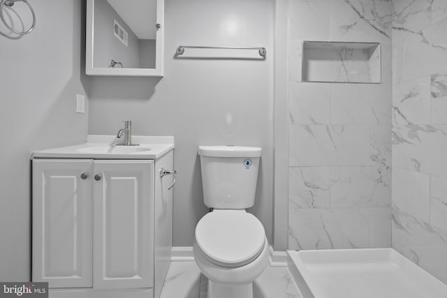 bathroom with tiled shower, vanity, and toilet