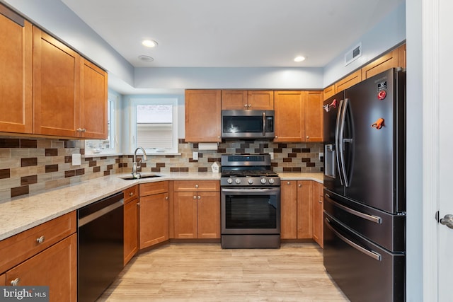 kitchen featuring appliances with stainless steel finishes, sink, decorative backsplash, light stone counters, and light hardwood / wood-style flooring