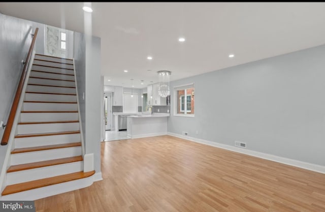 unfurnished living room with wood-type flooring, sink, and a notable chandelier