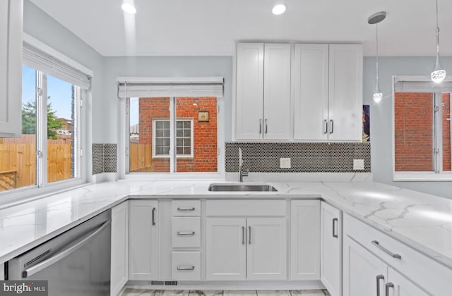 kitchen featuring pendant lighting, sink, dishwasher, light stone counters, and white cabinets