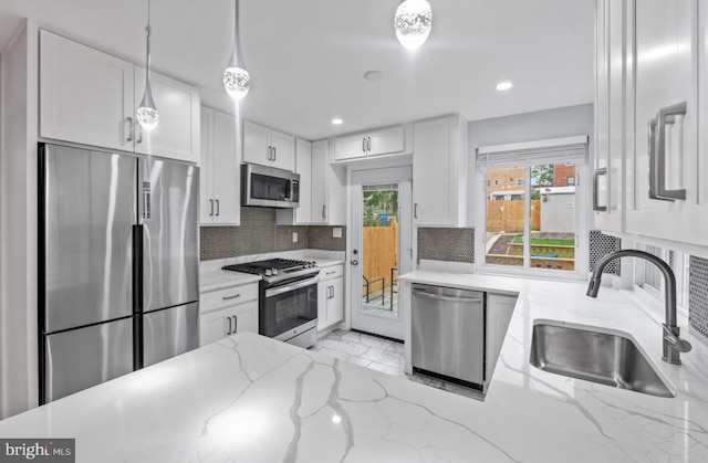 kitchen with sink, appliances with stainless steel finishes, hanging light fixtures, light stone counters, and white cabinets