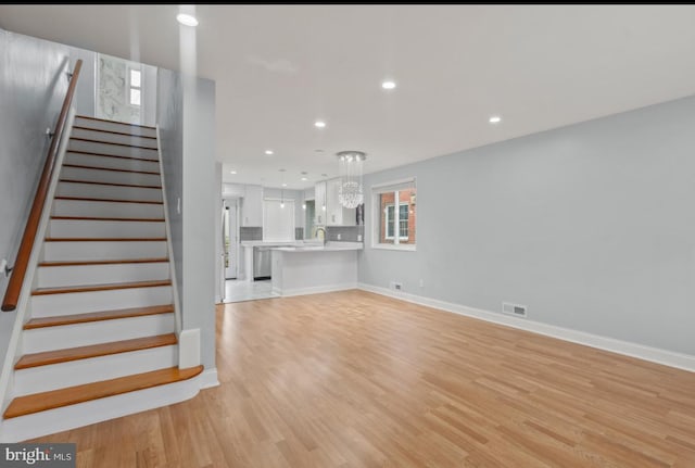 unfurnished living room featuring an inviting chandelier, sink, and light hardwood / wood-style floors