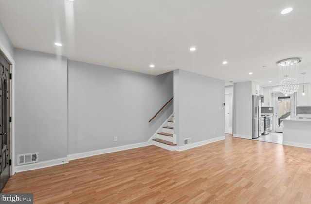 unfurnished living room featuring an inviting chandelier and light hardwood / wood-style flooring