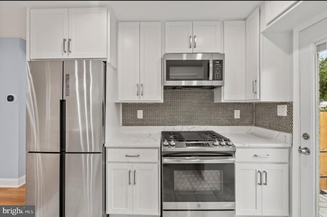 kitchen with white cabinetry, tasteful backsplash, light wood-type flooring, appliances with stainless steel finishes, and light stone countertops