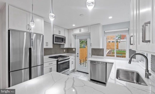 kitchen with appliances with stainless steel finishes, sink, white cabinets, hanging light fixtures, and light stone countertops