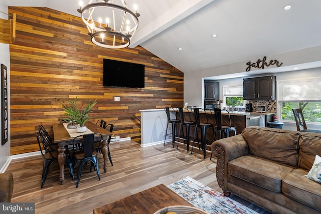 living room featuring vaulted ceiling with beams, wooden walls, light wood-type flooring, and a notable chandelier